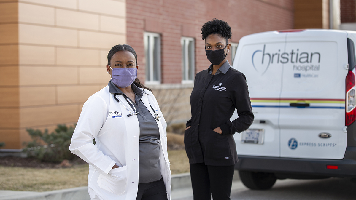 Connie Douglas, ANP-BC, pictured with Brittany Betts, community health worker. Looking at camera with a Christian Hospital ambulance and the hospital in the background.